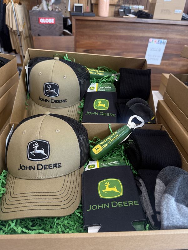 Open gift box featuring a tan John Deere trucker cap, black can cooler, green bottle opener, and black socks