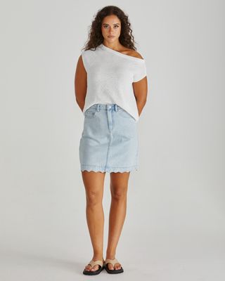 Full-length front view of the white knitted Jaci top paired with a light blue denim mini skirt