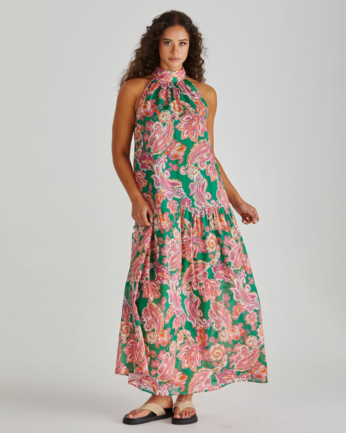 Elegant flowy maxi dress in vibrant green and pink paisley print, featuring a high halter neckline and tiered skirt.