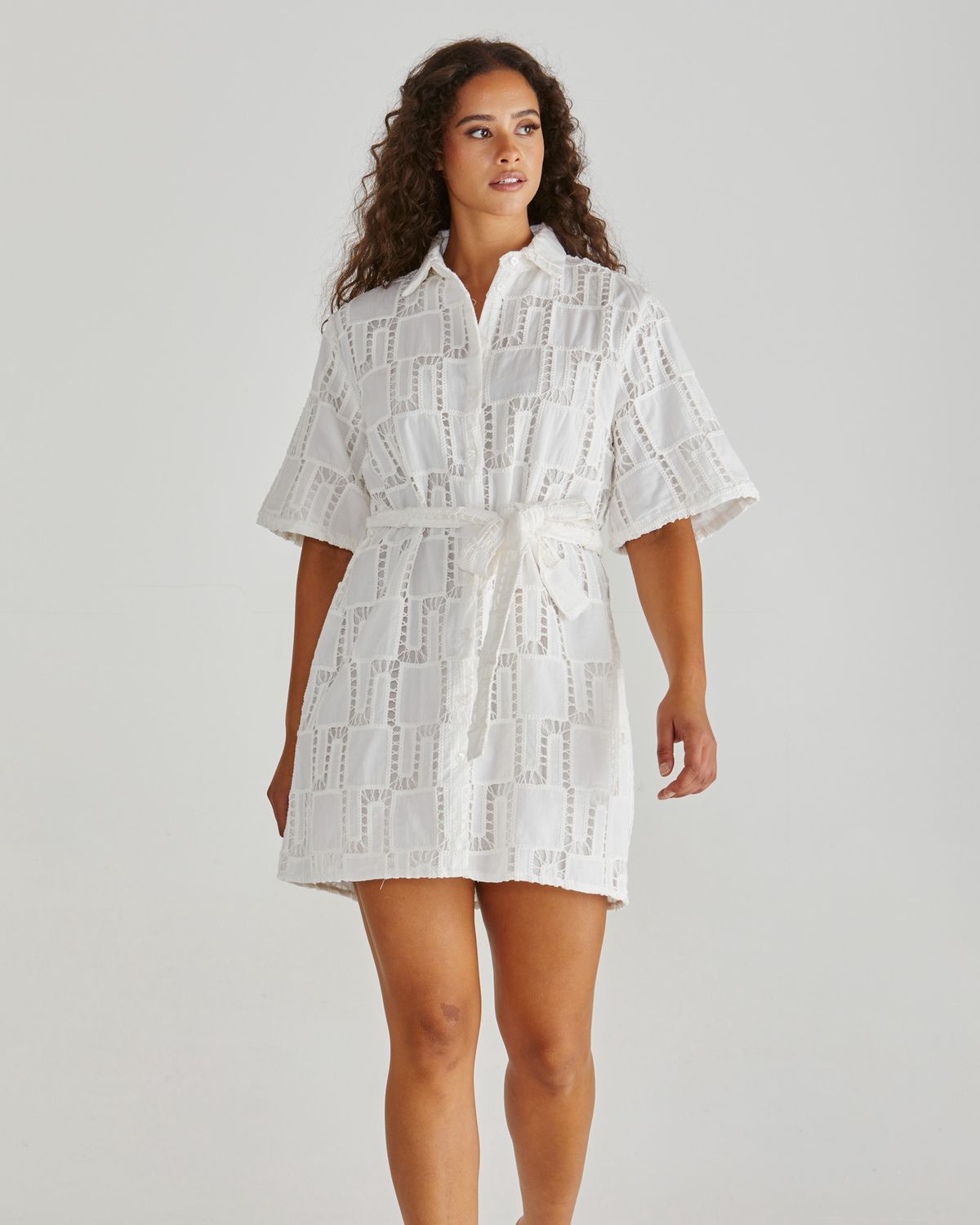 Model wearing the white Sass Dillon shirt dress, showcasing the intricate cut-out broderie pattern and tie-waist detail.