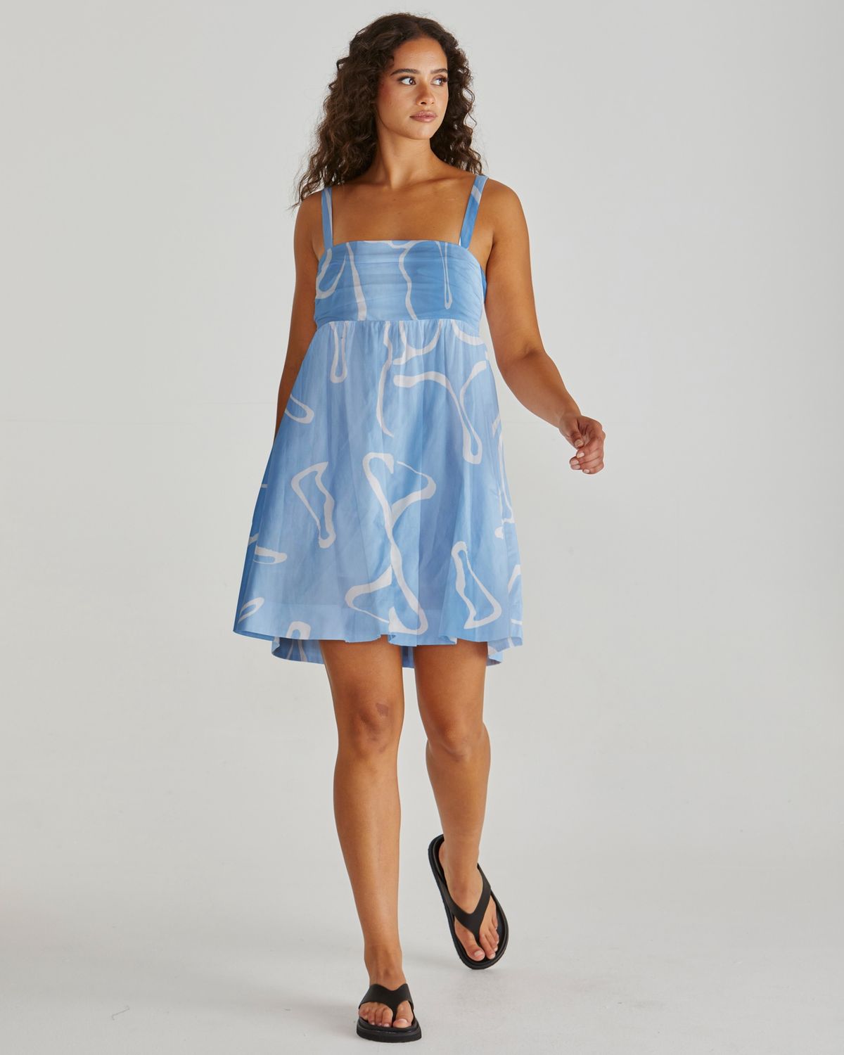 Full-length shot of a model wearing the Sass Tilda empire line mini dress in a striking blue colour with an white wave