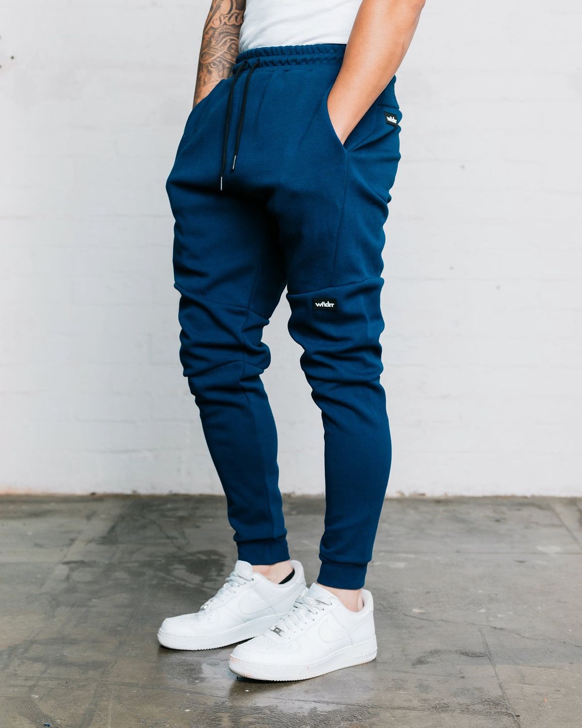a man wearing the navy blue WNDRR trackpants showing the details and pockets on the side