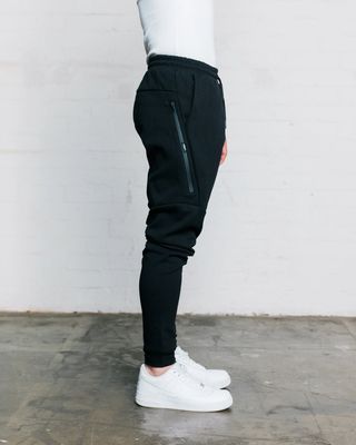 A side profile of the WNDRR black trackpants showing the cuffed bottoms and black zip pockets on the side