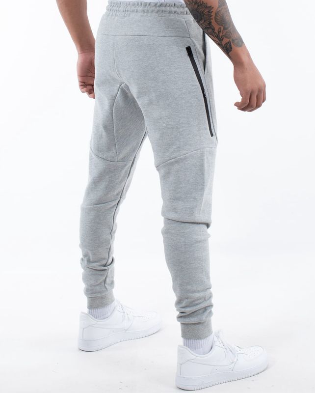 Back view of man wearing light grey WNDRR trackpants with zippered pockets 
