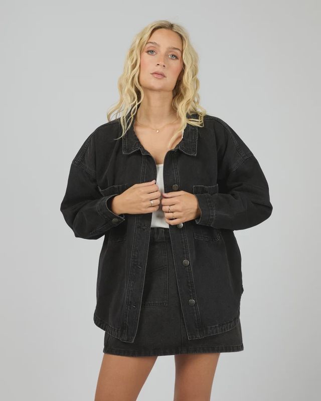 Model wearing the oversized All About Eve Dale Shacket in washed black denim, styled open over a white top and skirt.