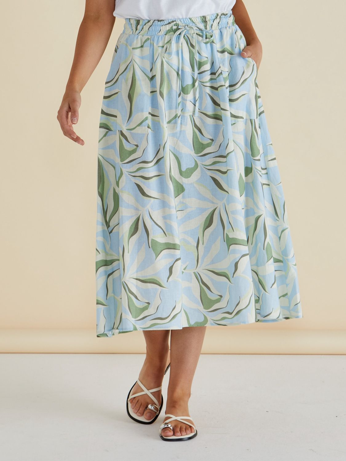 Close-up of a blue and green abstract leaf print midi skirt featuring a shirred elastic waistband, worn with white sandals.
