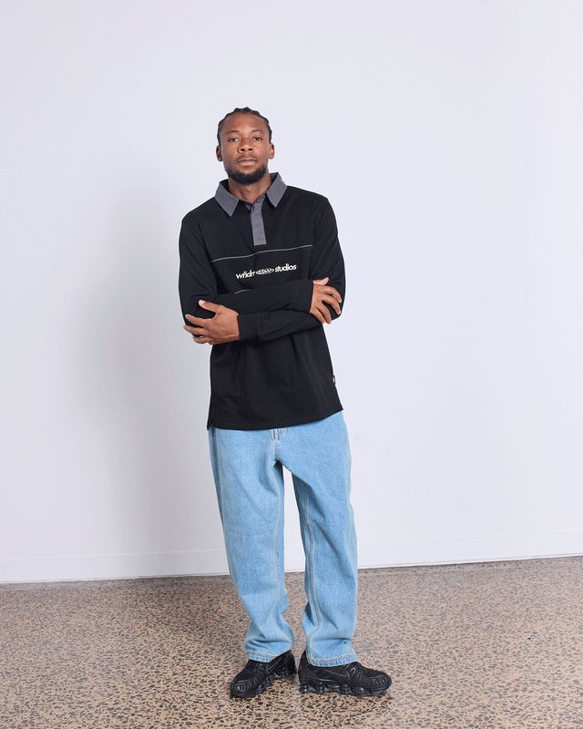 Full body view of a man wearing the Wndrr Globe Rugby Polo Shirt featuring a collar and cuffed sleeves. Wearing with bluejean