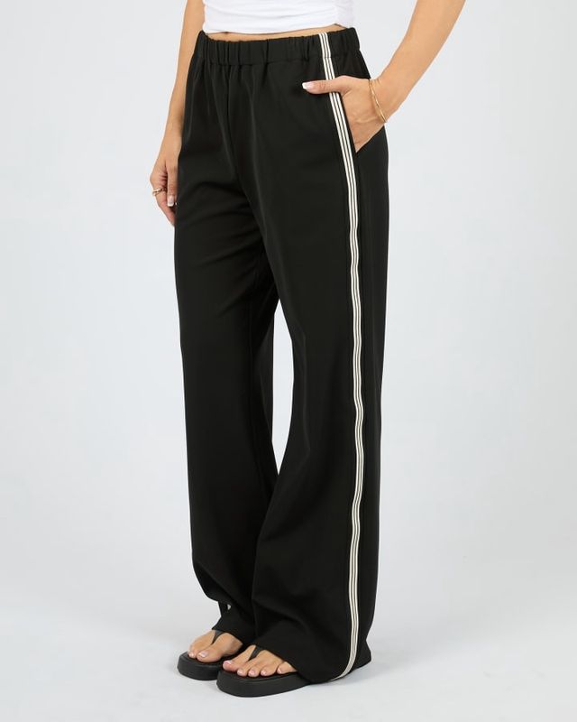 Side view of a women wearing the Lina Pant in Black from All About Eve featuring pockets and black a white stripes down leg