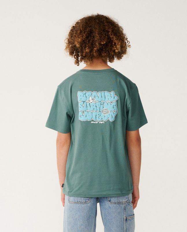 A back view of a boy model wearing the Surf Shack Tee [8-16YEARS] featuring a large Surf Shack puff  logo on the back.