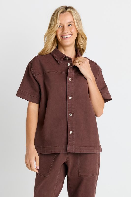 A female model wearing the Betty Basics Quinn Cotton Shirt, featuring a chocolate colour, sliver button up and collar.