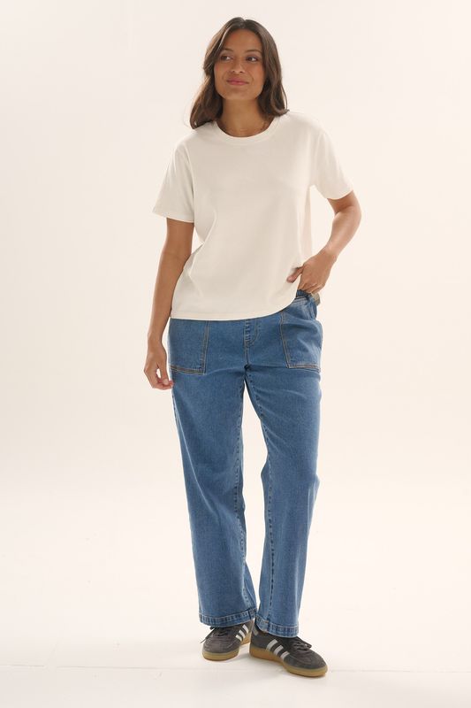 Full body view of a female model wearing the Betty Basics Base Tee in White matching it back with a pair of denim jeans.