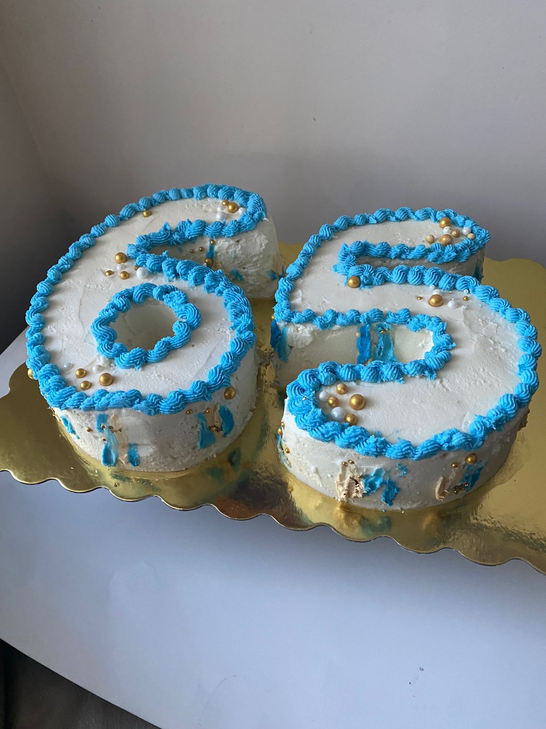 Elegant cake shaped as the number 65, with a white base, and gold and blue decorative elements for a striking birthday celebration.