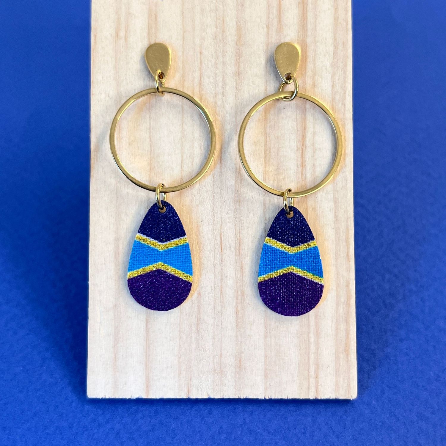 boucle d'oreille Bleu nuit, violet et turquoise sublimés par des lignes dorées dans un motif graphique et dynamique.