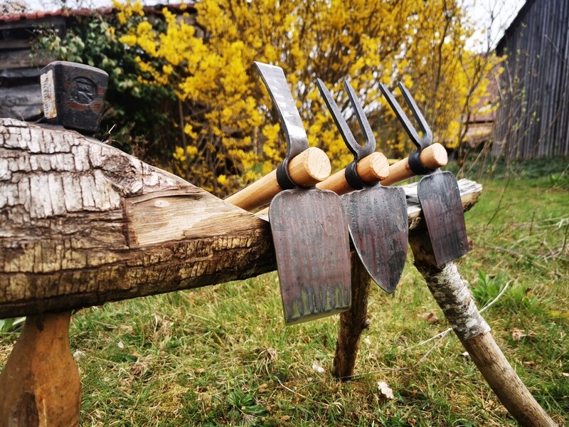 Trois modèles de serfouettes, (panne large et panne étroite, panne large et crochet, langue et crochet) posées sur un chevalet en bois dehors.