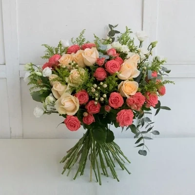 Букет составлен из оранжевых и персиковых роз и декоративной зелени.
