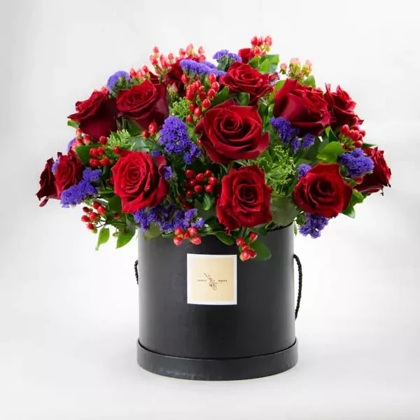 The composition uses red roses, statice, and hypericum.

