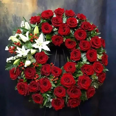 Большой траурный венокс красными розами и лилиями, опорой для рамы и траурной лентой. Средний диаметр этого венка 50 сантиметров