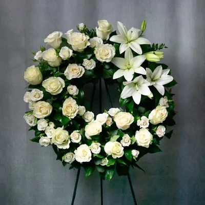 A large funeral wreath with white lilies, frame support, and a funeral ribbon. The average diameter of this wreath is 50 centimeters