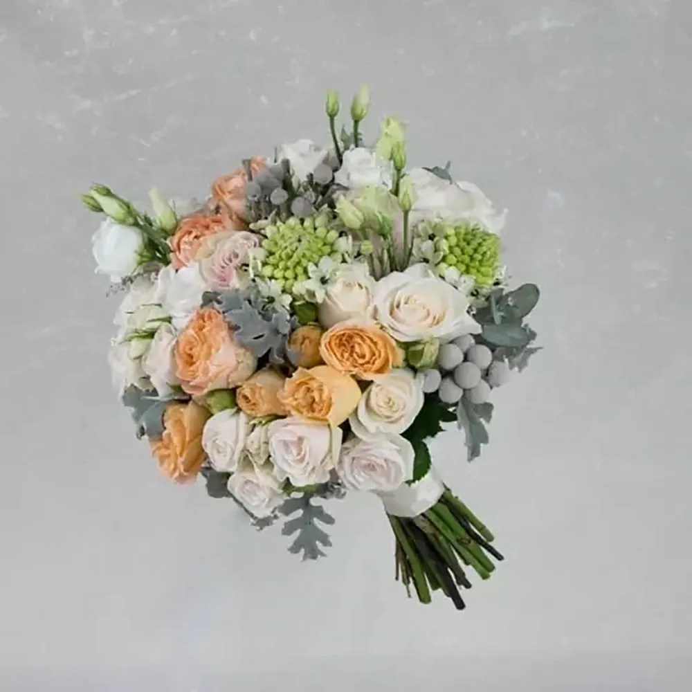 The wedding bouquet consists of a mix of flowers in peach green and white tones