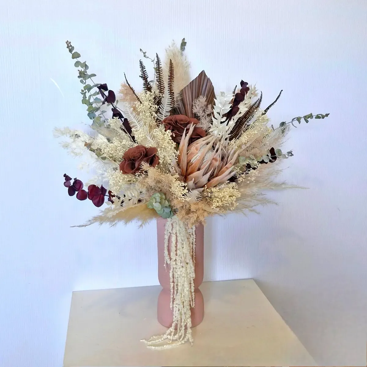Dried flower arrangement in a ceramic vase featuring a red preserved rose, protea and mixed foliage.