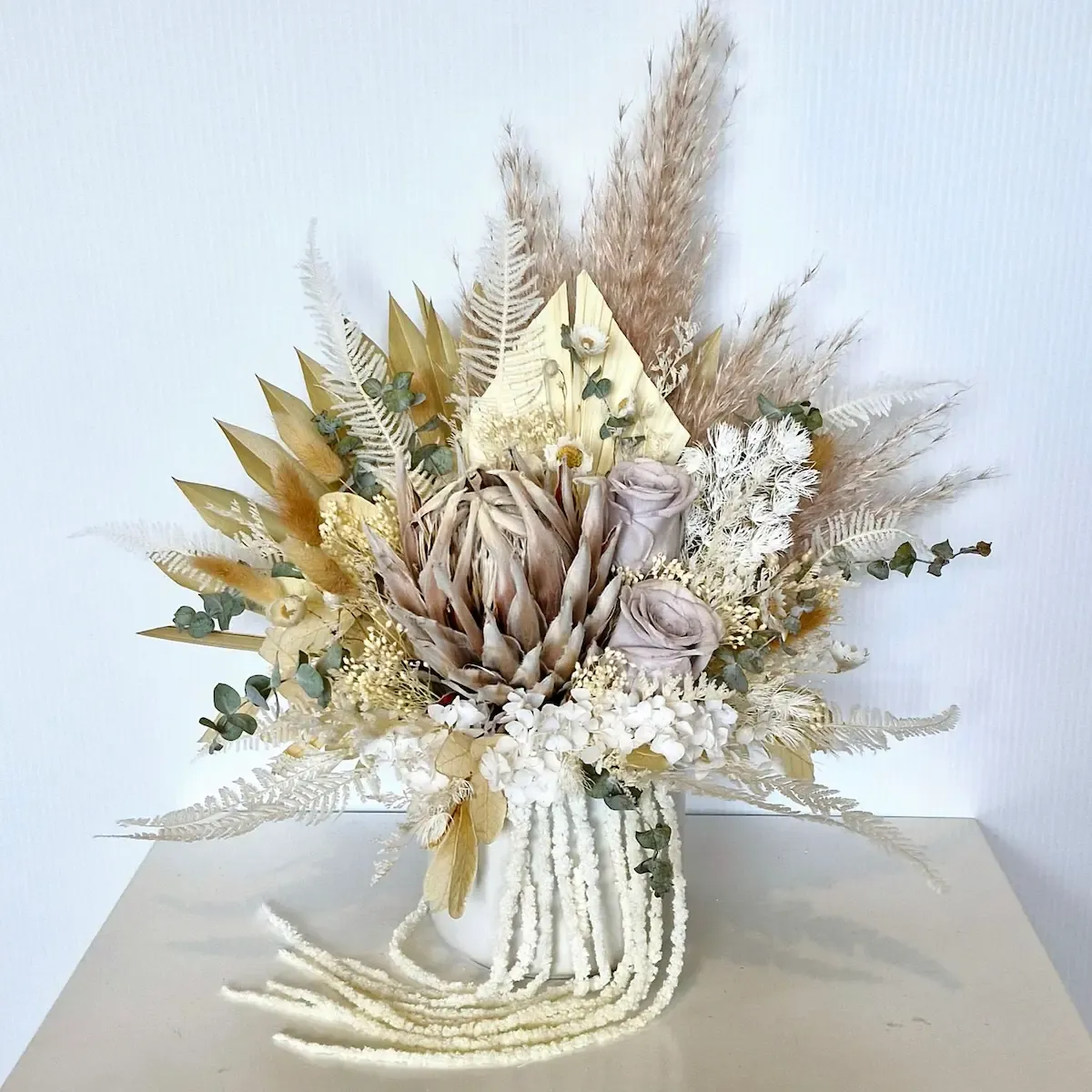 Neutral dried flower arrangement in a white ceramic pot with king protea, roses, hydrangea and soft preserved foliage.