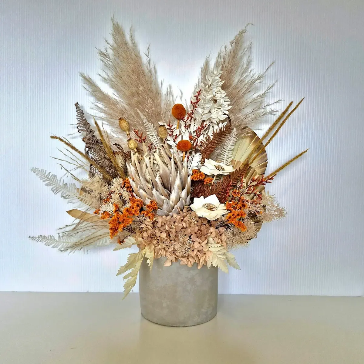 Ember dried flower arrangement with king protea and burnt orange tones in a concrete pot.
