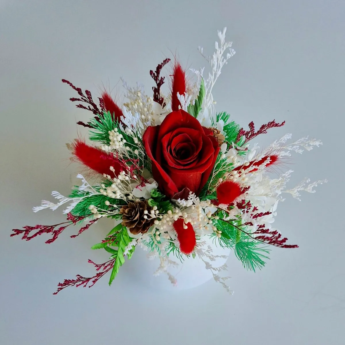 Christmas dried flower arrangement in a pot with a preserved rose, bunny tails, limonium, pinecone and festive foliage.