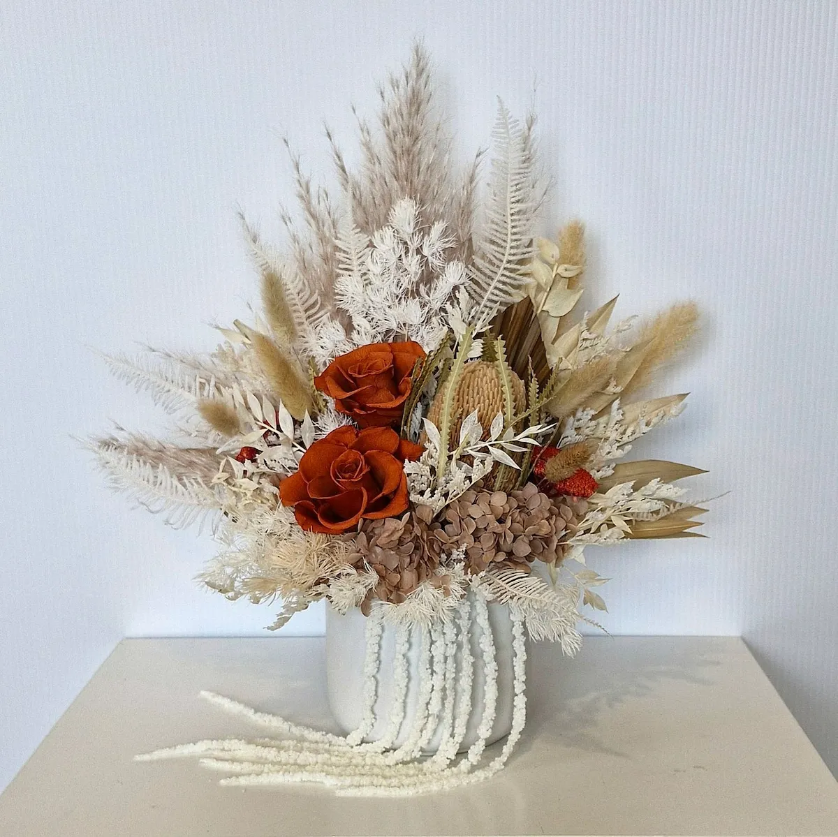 Fireglow dried floral arrangement in white ceramic pot with burnt orange and neutral preserved flowers.