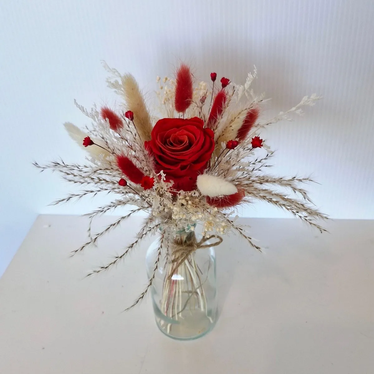 Small Flirt dried flower arrangement in glass vase with red rose, bunny tails, and star flowers.