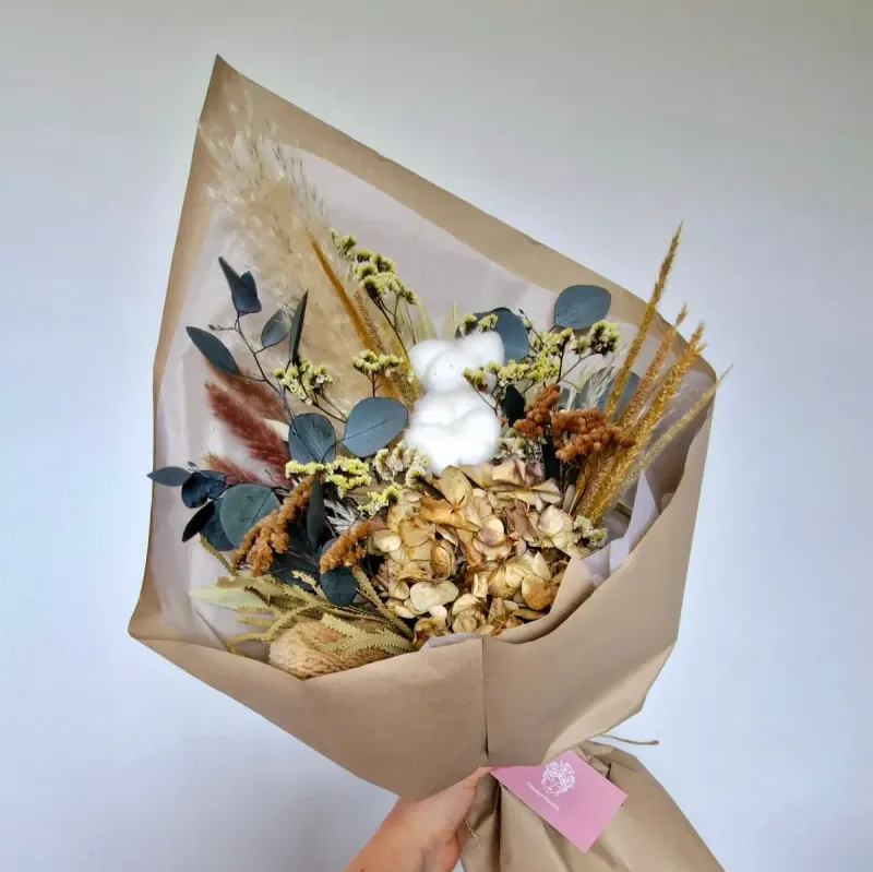Earthy dried floral bouquet shown at an angle, featuring neutral hydrangea, banksia, cotton stems, and grasses.