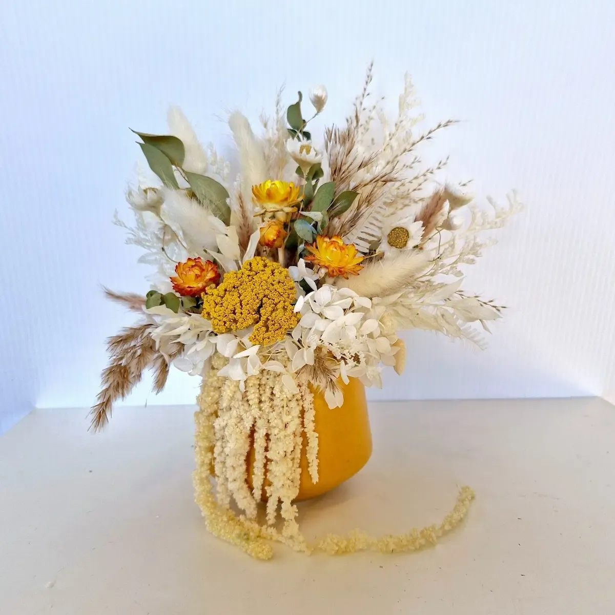 Cozy dried floral arrangement in mustard ceramic pot with yellow and natural preserved flowers.