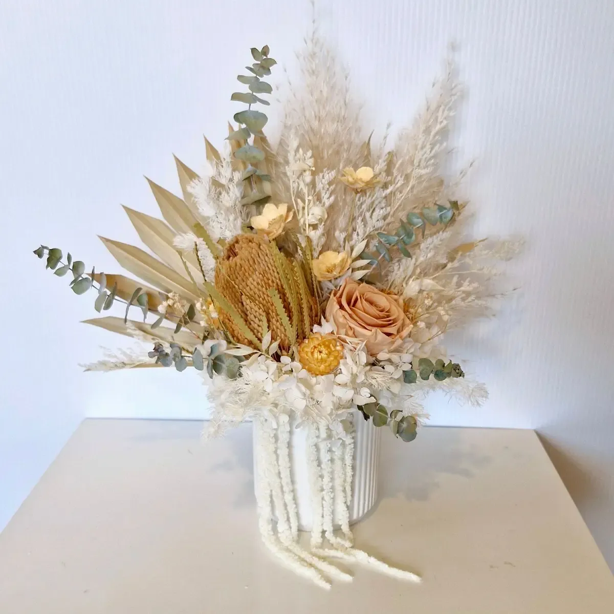 Cinnamon dried floral arrangement in white ceramic pot with neutral-toned preserved roses, hydrangea and foliage.