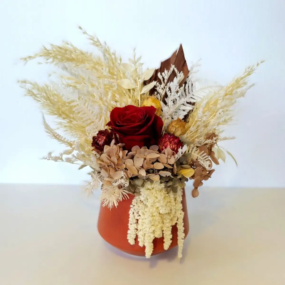 Charisma dried flower arrangement in ceramic pot featuring red rose, hydrangea, amaranthus and preserved foliage.