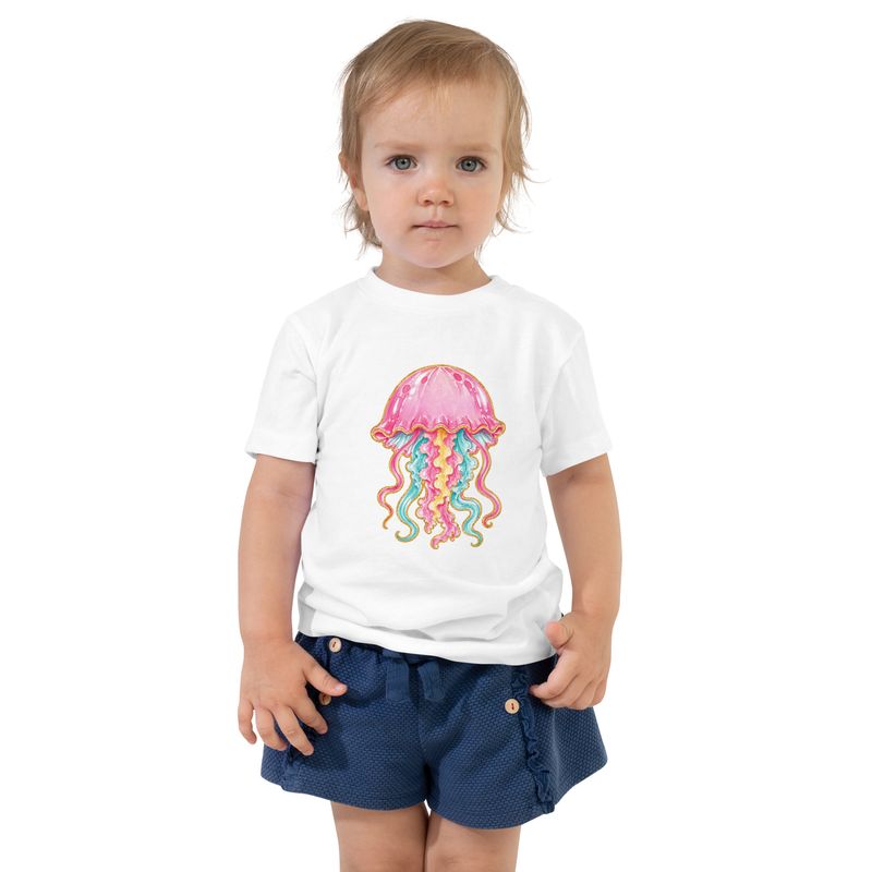 Smiling young girl wearing a white toddler T-shirt with a colorful pink jellyfish graphic and denim shorts.