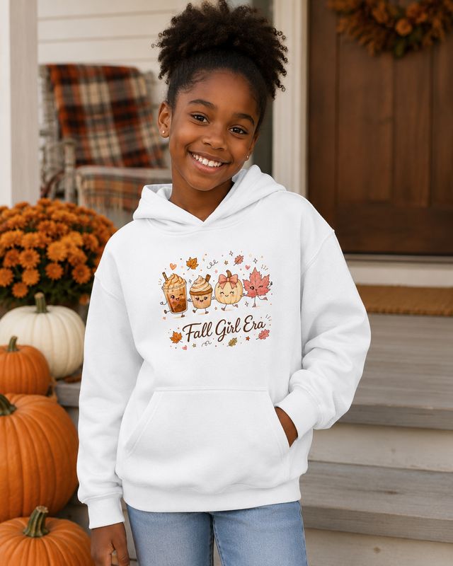 Smiling Black girl in a white Fall Girl Era hoodie on a fall porch decorated with pumpkins.
