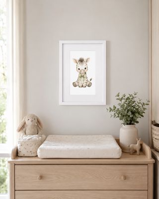 Framed watercolor baby zebra print above a light wood changing table in a neutral nursery.