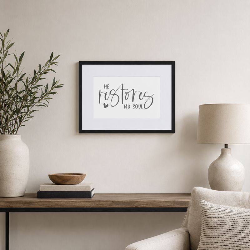 Small black framed “He Restores My Soul” Christian wall art displayed in a bright neutral living room.