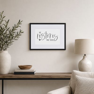 Small black framed “He Restores My Soul” Christian wall art displayed in a bright neutral living room.
