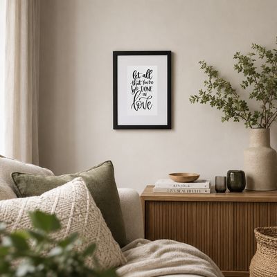 21×30 cm black framed Bible verse print, “Let all that you do be done in love,” styled in a neutral living room.