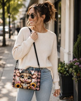 Woman in a cream sweater and sunglasses wearing a pink Highland cow crossbody bag outdoors.