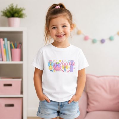 Girl wearing a size 3-4 white organic cotton T-shirt with pastel pencil, apple, scissors, ruler, bows, and stars.