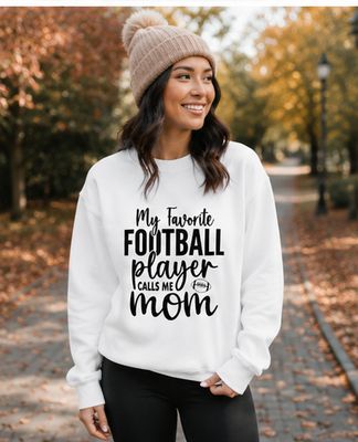 Woman wearing a white football mom sweatshirt and knit beanie on a scenic autumn walkway.