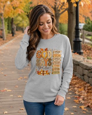 Woman wearing a gray God Says You Are Christian long-sleeve shirt on an autumn park walkway.