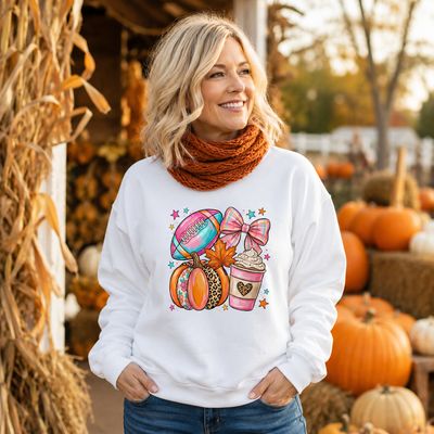 Blonde woman wearing a white football and pumpkin sweatshirt with an orange scarf at a pumpkin patch.