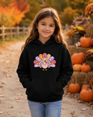 Girl in a kids medium black hoodie with a colorful Thanksgiving turkey graphic at an autumn pumpkin patch.