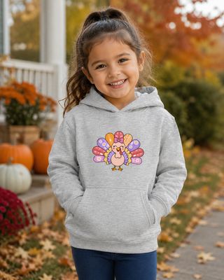 Young girl in a kids small athletic heather hoodie with a colorful turkey graphic in a festive fall setting.