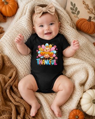 Baby girl in black 3–6 month Thankful turkey bodysuit on a cozy fall blanket with pumpkins.