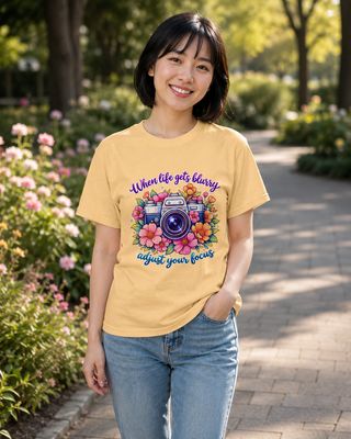 Petite East Asian woman wearing a yellow haze floral camera T-shirt with “When life gets blurry, adjust your focus” quote.