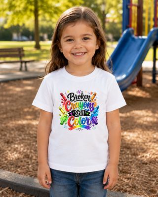Young girl in white Broken Crayons Still Color T-shirt smiling at a sunny playground near a blue slide.
