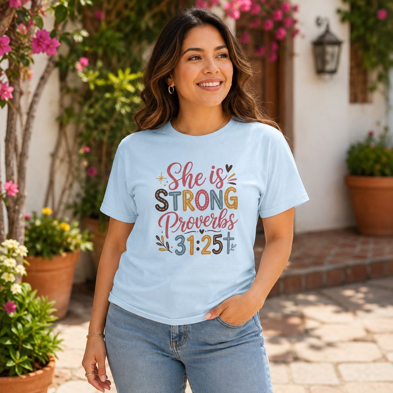 Latina woman wearing a light blue “She Is Strong” Proverbs 31:25 Christian T-shirt in a sunny flower courtyard.